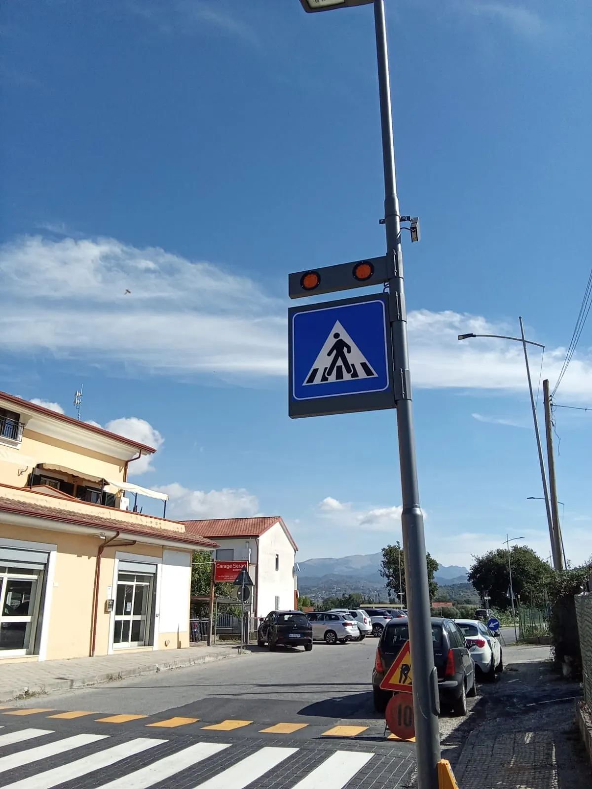Segnale verticale di attraversamento pedonale con lanterne luminose, installato su palo a bordo strada